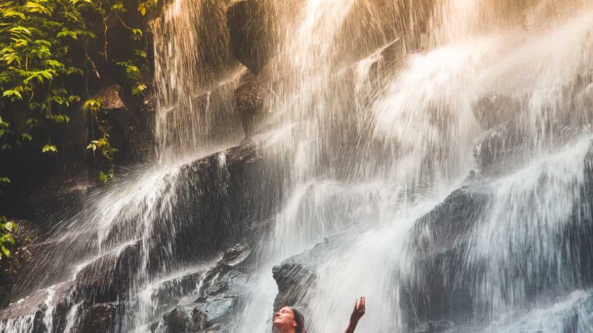 Woman meditating on rocks in front of a waterfall